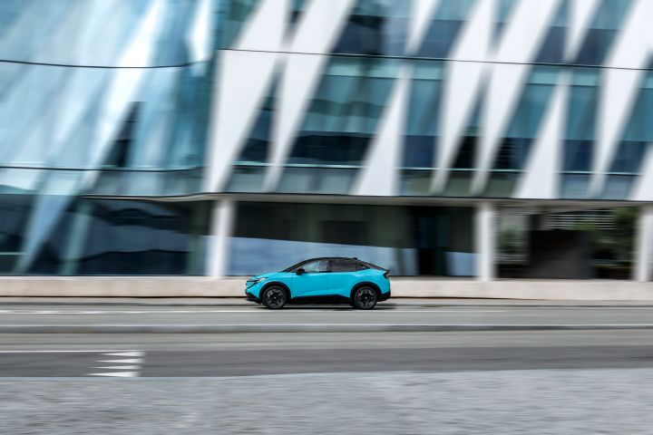 Seitliche Fahraufnahme eines Nissan LEAF vor einer großen hellen Gebäudefassade, die durch die Geschwindigkeit leicht verschwimmt