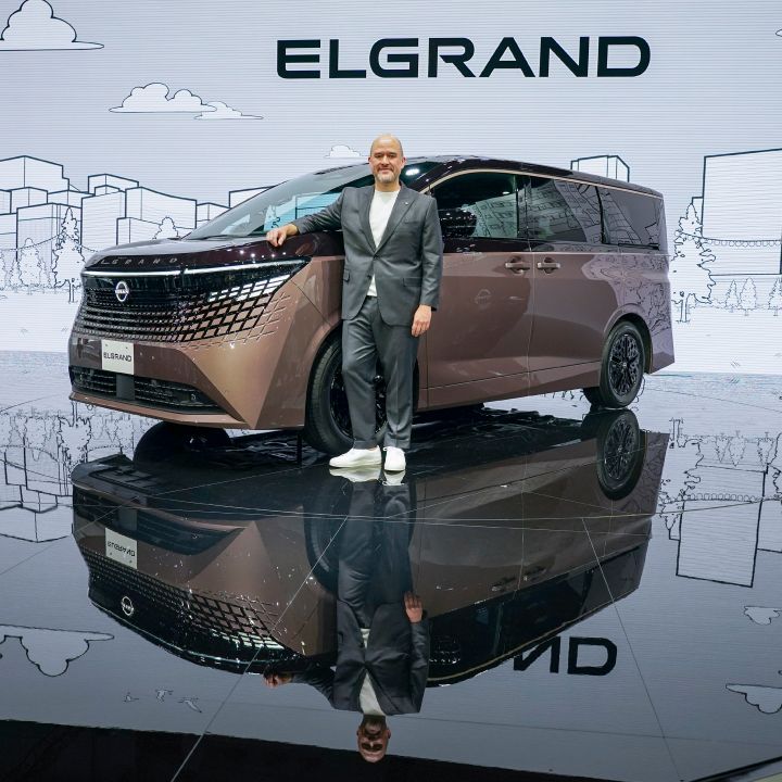 On the stage, the all-new Elgrand in Fuji Dawn and Shigoku two-tone colors is positioned diagonally, facing slightly to the left. Next to the vehicle stands CEO Ivan Espinosa in a suit, resting one hand on the car while posing. The background features a white screen with cityscape line art and the text ELGRAND.