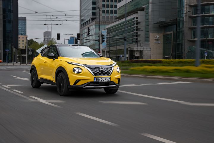 Jadący żółty Nissan Juke (widok z półprofilu) z budynkami w tle