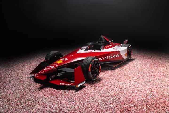 Front left 3/4 view of a red and white Nissan Formula E Racecar under a spotlight in a dark room.