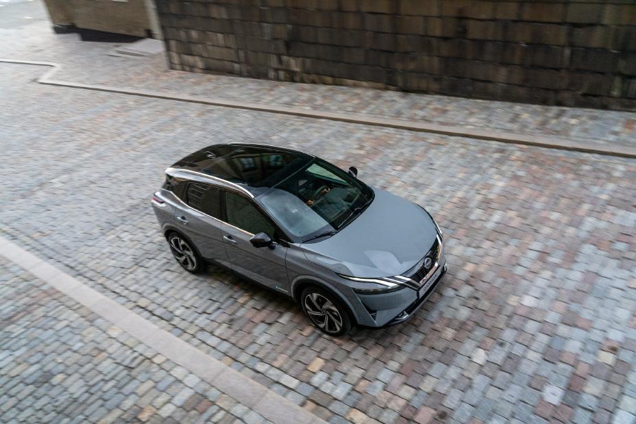 Extérieur gris Nissan QASHQAI de trois quarts roulant sur une route en pente.