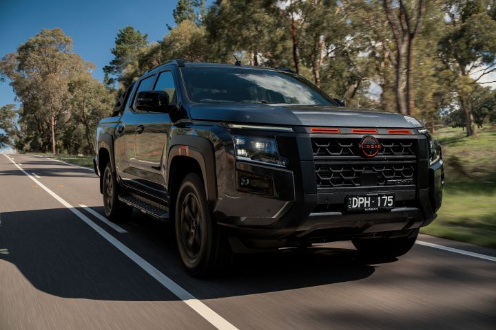 2026 Nissan Navara PRO-4X finished in Boulder Grey featured in a tracking image through eucalyptus trees with black honeycomb grille, daytime lamps and planted stance.