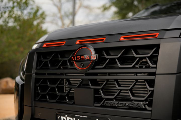 2026 Nissan Navara PRO-4X finished in Boulder Grey showing a close-up of the black grille with Nissan badge, red accents and PRO-4X branding.