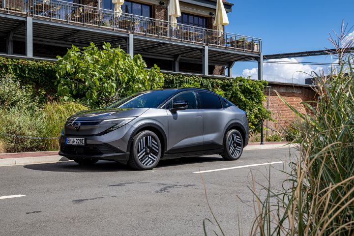 Im Sonnenschein steht ein grauer Nissan Leaf vor einem zweigeschossigen Backsteingebäude mit mehreren Balkonen