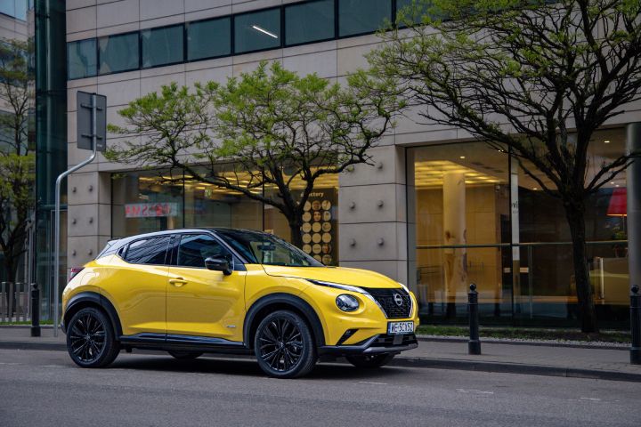 Żółty Nissan Juke stojący bokiem na tle budynku i drzew