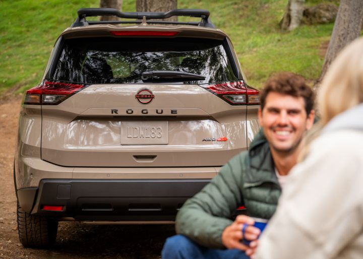 Rear view of a 2025 Nissan Rogue rock creek parked on a campsite with 2 people in coats smiling to each other.