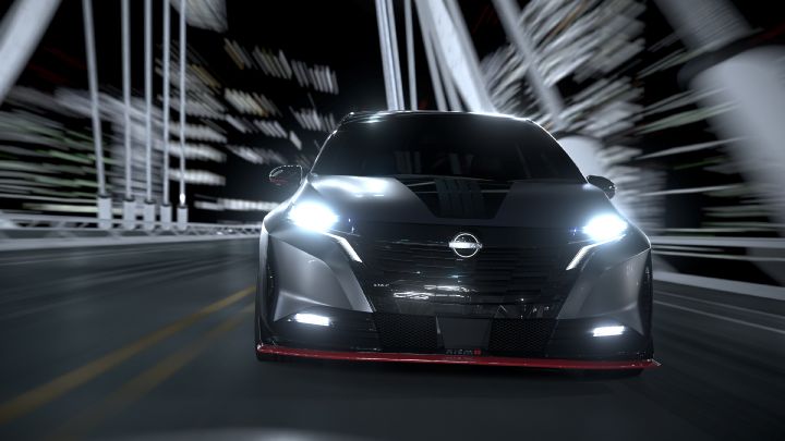 A silver and black two-tone sports car, the Aura Nismo RS Concept, viewed head-on as it speeds across a bridge. The vehicle is moving straight ahead with bright headlights shining. The front grille features the Nissan logo, and a red accent line runs along the lower bumper. The background shows streaks of light, emphasizing speed and dynamic motion