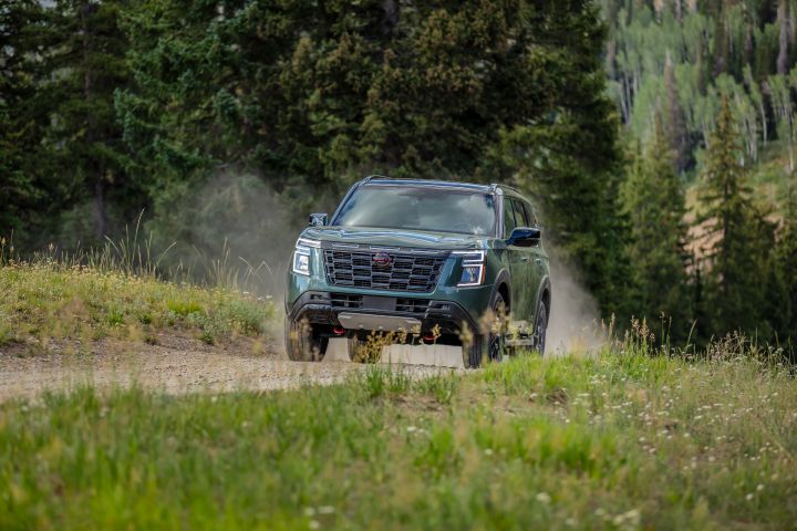 Angled front view of a 2025 Nissan Armada driving on a dirt path in the woods, dust is flying up behind to indicate speed.