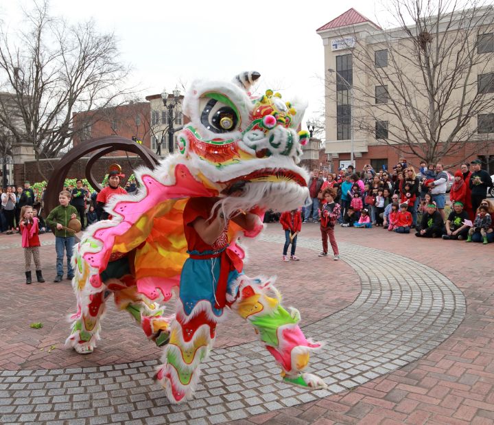 A person in a traditional dragon costume walking through a large group of kids on a cloudy day.
