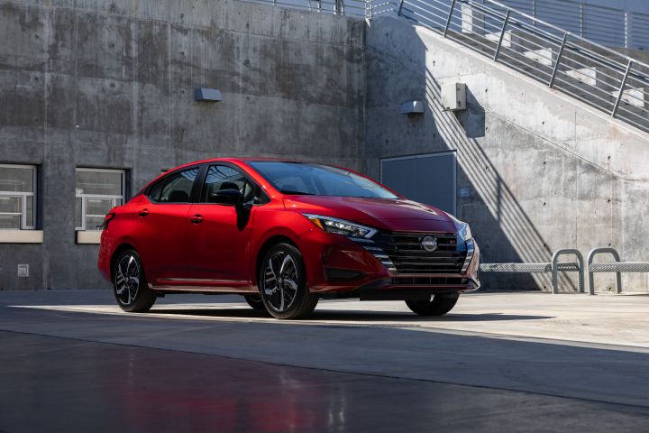 A red Nissan Versa parked at a concrete building