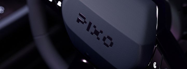 Photograph shows close-up of a black steering-wheel with a PIXO logo.