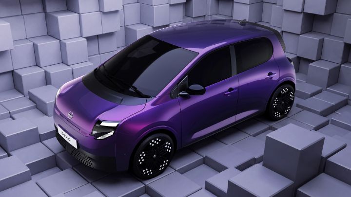Photograph showcasing a purple Nissan PIXO compact hatchback displayed within a geometric room of gray cubes. Black panoramic roof, dark windows, illuminated headlights, patterned wheels, and white front license plate create a sleek concept-car presentation.
