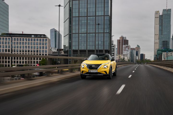 Jadący żółty Nissan Juke (widok z przodu) z budynkami w tle