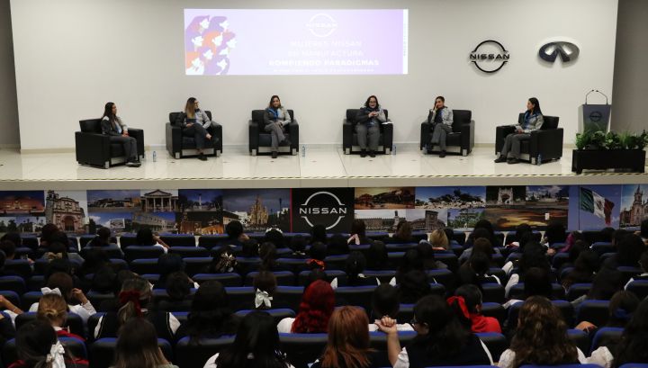 Foto de las 6 mujeres panelistas sentadas en el escenario del salón de eventos de Planta A1 de Manufactura, se visualiza parte de la Audiencia, en su mayoría mujeres
