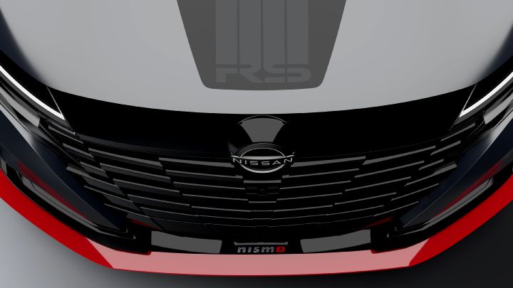 A close-up studio shot of the front section of the Aura Nismo RS Concept, a silver and black two-tone sports car. The image features a black front grille with the Nissan logo at the center, a red accent line with the 'NISMO' logo on the lower bumper, and black stripes with an 'RS' logo on the hood. The background is a simple gray, highlighting the car's detailed design.