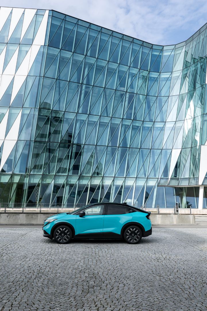 Vor einem modernen Gebäude mit gläserner Fassade parkt seitlich ein türkiser Nissan LEAF