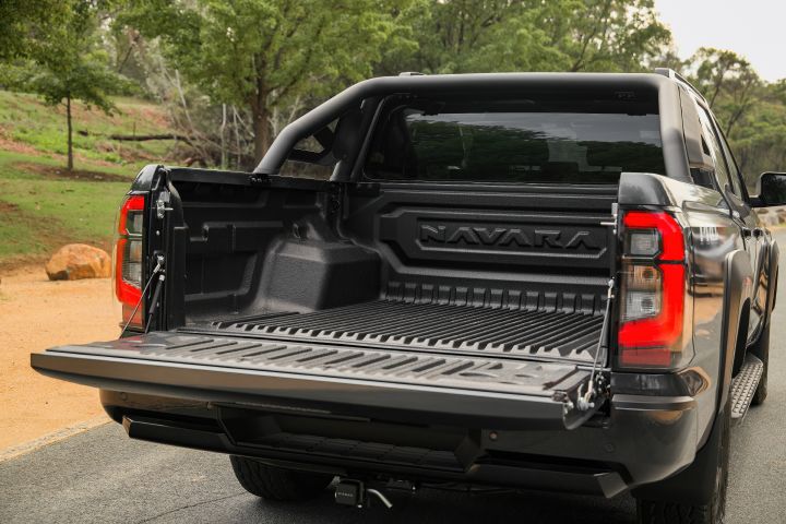 2026 Nissan Navara PRO-4X finished in Boulder Grey shown from the rear three-quarter angle with lowered tailgate, open tub and towing hardware.