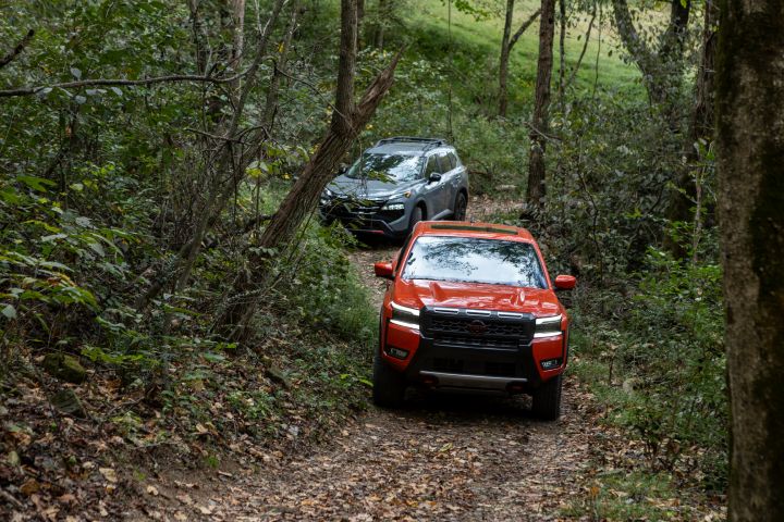 A Nissan Rogue and Frontier trail through a narrow path in the woods.