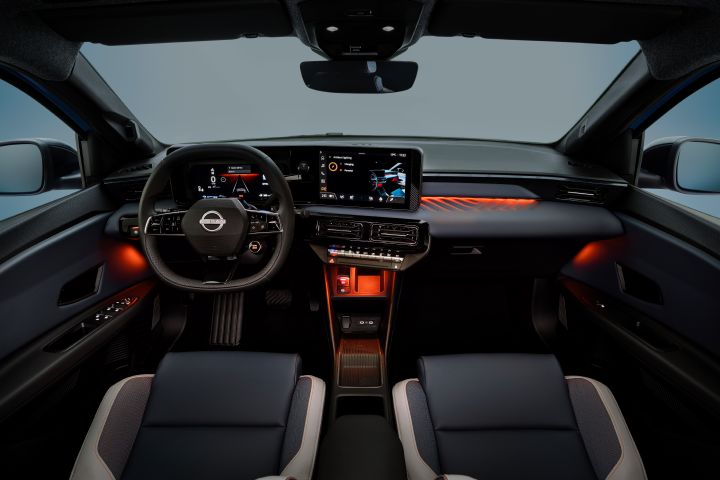 dimmed interior of Micra dashboard and cockpit from driver's POV revealing orange ambient lighting by side doors, on dashboard and below air conditioning buttons.  steering wheel, front seats and infotainment in view