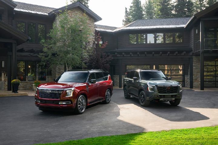 A red and a dark green 2025 Nissan Armada parked at opposing angles in front of an upscale cabin.