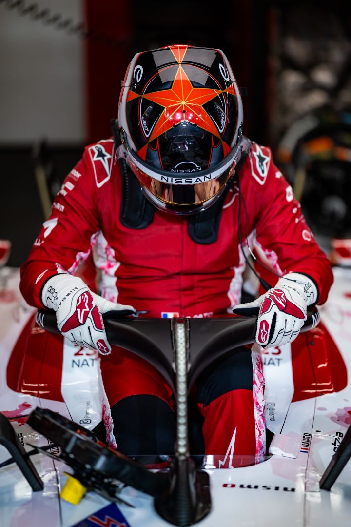 Norman Nato steigt in einem roten Rennanzug und mit Helm ins Cockpit seines Nissan Formel-E-Rennwagens. Das Fahrzeug ist überwiegend rot und weiß, im Hintergrund ist der Nissan Boxenbereich zu sehen.