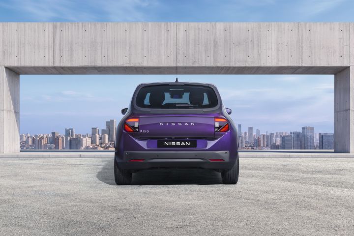 Vista traseira de um Nissan PIXO elétrico urbano, de cor roxa, estacionado debaixo de uma estrutura moderna de betão, com o horizonte da cidade ao fundo.