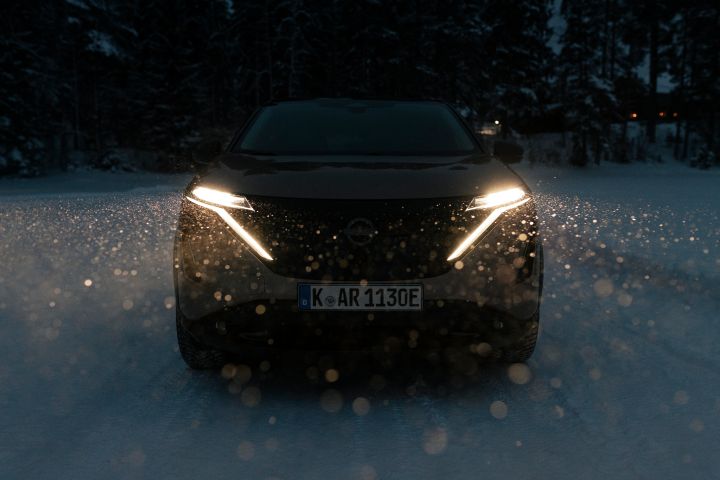 Elektroauto Nissan Ariya e‑4ORCE fährt im Dunkeln auf schneebedeckter Straße mit eingeschalteten Scheinwerfern, Front