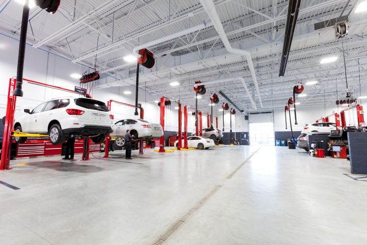 Un centre de service automobile spacieux et moderne avec plusieurs véhicules élevés sur des ascenseurs rouges pour l'entretien.