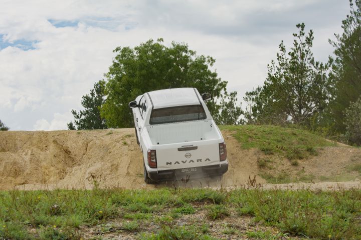 2026 Nissan Navara SL dual cab ute finished in Alpine White viewed from the rear while descending a sandy slope, featuring the NAVARA tailgate and dust from the tyres.