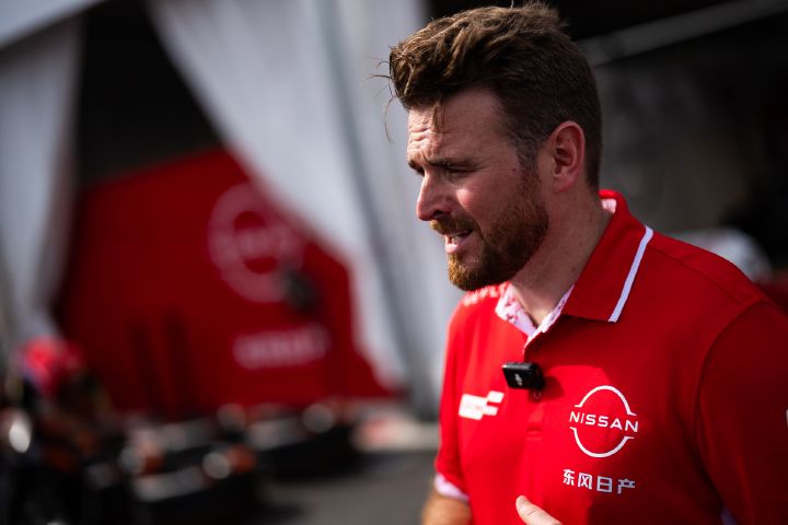 Seitenansicht von Oliver Rowland, der sein rotes Team-Polohemd trägt und vor der Teamgarage spricht.