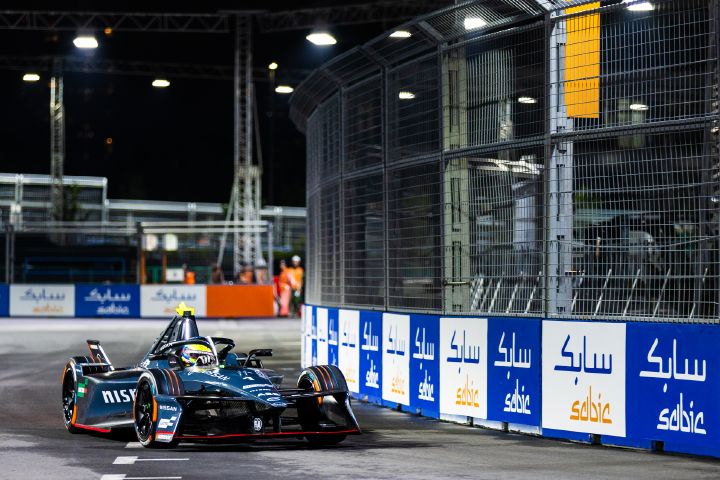 Oliver Rowland biegt mit dem Auto Nr. 1 in Sonderlackierung beim E-Prix in Tokio nach links ab, während auf der Innenseite der Kurve blau-weiße Werbetafeln zu sehen sind.