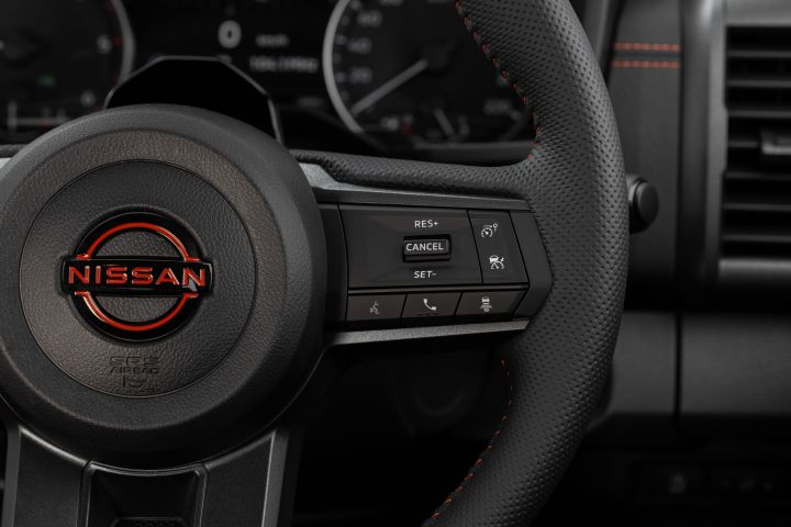 2026 Nissan Navara PRO-4X finished in Boulder Grey highlighting the steering wheel with Nissan badge, perforated leather rim and right-side cruise-control buttons.