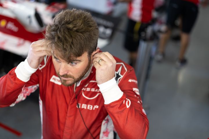 Oliver Rowland steckt sich in der Teamgarage, gekleidet in seinen roten Rennanzug, seine Ohrhörer ein.