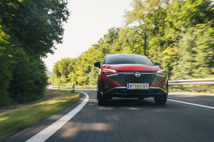 Frontaufnahme eines fahrenden Nissan Qashqai in Fuji Sunset Red auf einer baumbestandenen Landstraße