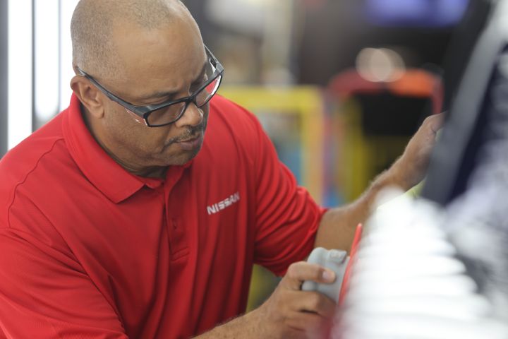 A man in a red Nissan shirt working on buffing the body of a car.