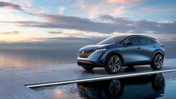 Un véhicule Nissan Ariya Concept bleu glacier est garé sur un quai en bois gris entouré d'eaux calmes. Un doux lever de soleil traverse l'horizon en arrière-plan.