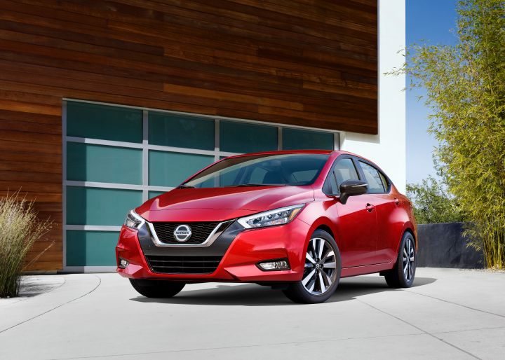 Front left view of a red 2021 Nissan Versa parked in front of a garage.