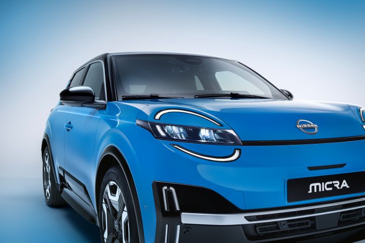 front side 7/8 view of Micra in gear blue color, signature headlamps, passenger side doors, micra badge and Nissan name plate