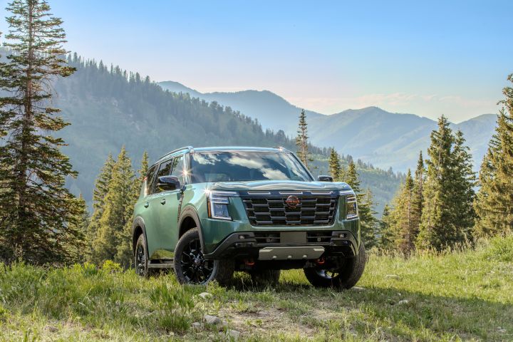 Tight front right 3/4 view of a 2025 Nissan Armada parked with its wheels turned on a grassy hilltop overlooking mountains.