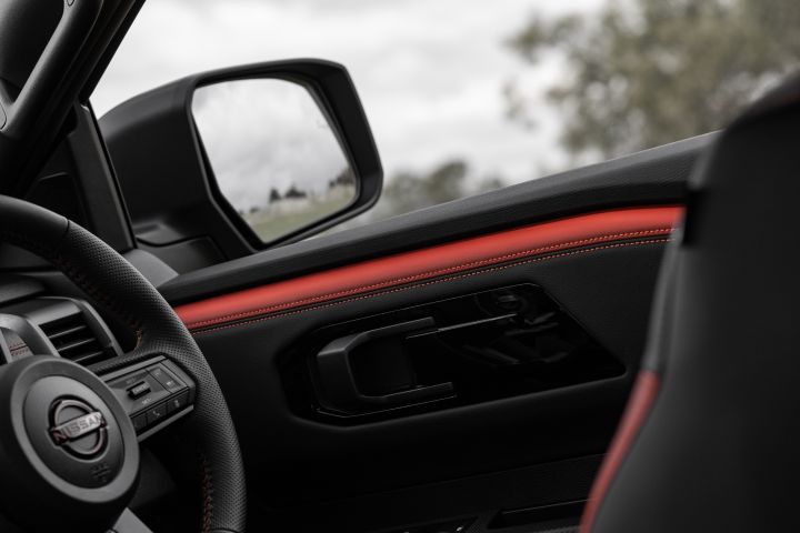 2026 Nissan Navara PRO-4X finished in Boulder Grey highlighting the driver-door trim, red stitched insert, black grab handle and exterior mirror.