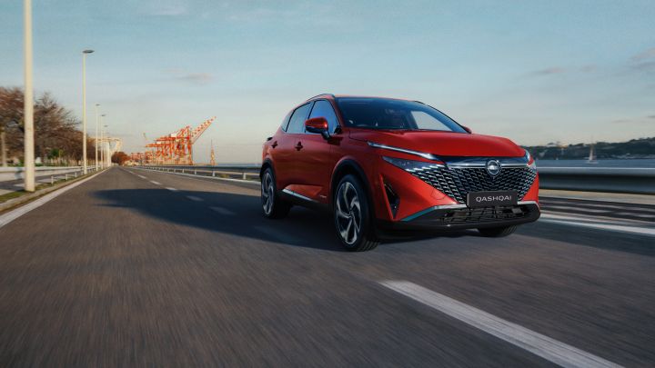 Front ¾ dynamic image of a red 2025 Nissan Qashqai Ti e‑POWER SUV driving down a highway