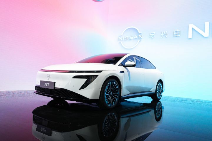 東風日産の白い新型セダン電気自動車「N7」の低位置からの正面図。背後にはピンクと青のスクリーン。