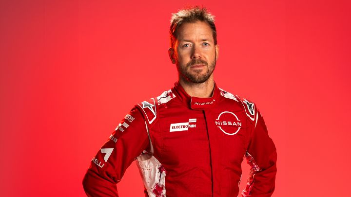 Bild im Querformat von Sam Bird, Ersatz- und Entwicklungsfahrer des Nissan Formula E Teams, der mit den Händen in den Hüften in seinem roten Team-Rennanzug vor einem roten Hintergrund steht.