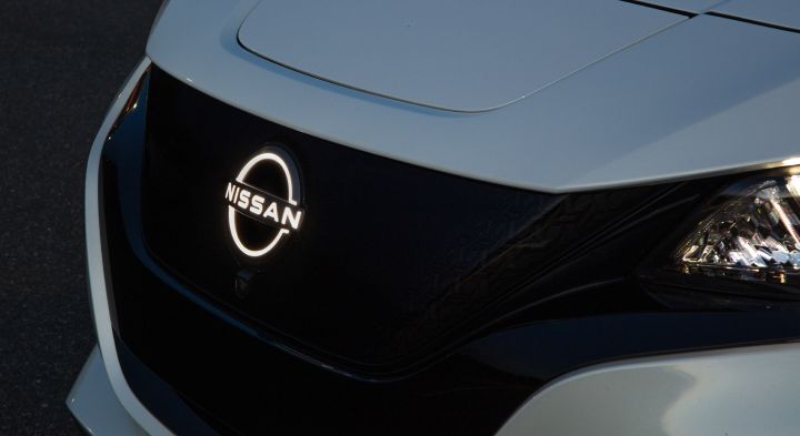 Close up of the illuminated Nissan logo on the grill of a white 2025 Nissan LEAF.