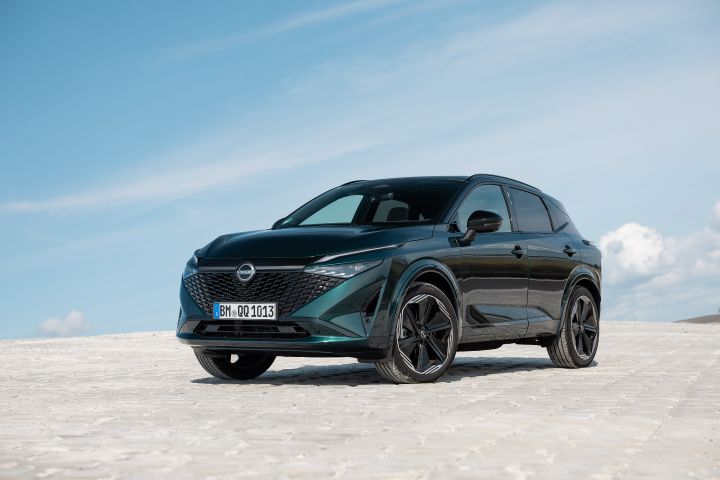 Blick von schräg vorne auf einen dunkelgrünen Nissan Qashqai, der an einem sonnigen Tag auf einem weißen Untergrund vor einem hellblauen Himmel steht