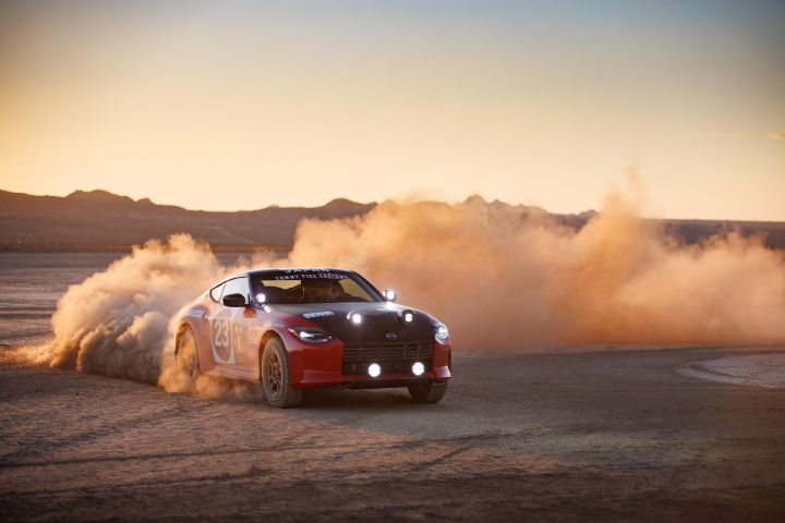 A Safari Rally Z Tribute with number 23 drives through dusty desert terrain at sunset