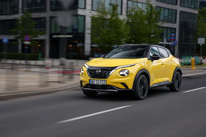 Jadący żółty Nissan Juke (widok z półprofilu) z budynkami w tle