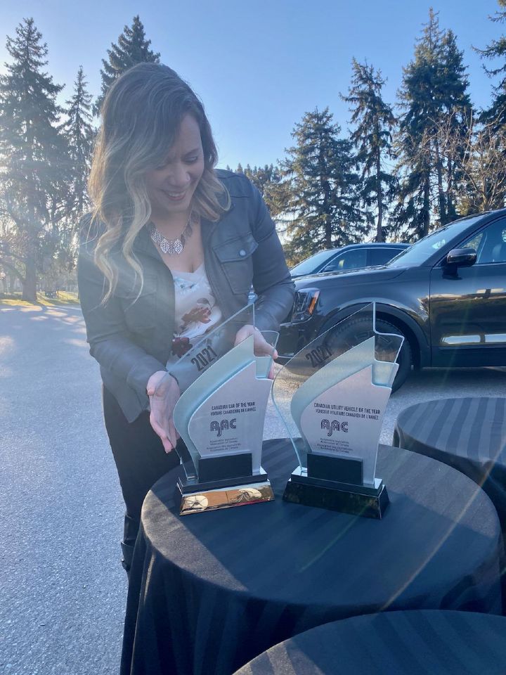 Woman posing with two awards outside.