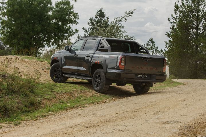 2026 Nissan Navara PRO-4X finished in Boulder Grey shown rear three‑quarter cresting onto a graded track with sports bar, side step and chunky tyres.
