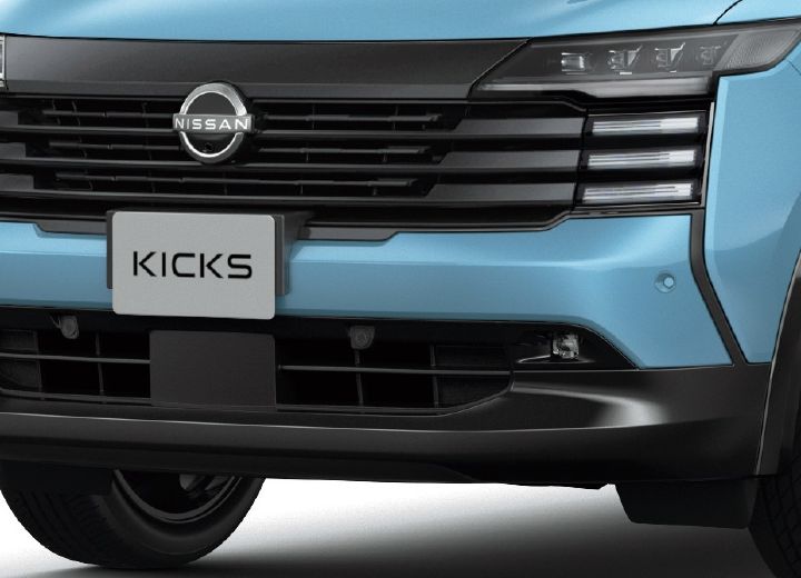 Close-up of the front center of a bluish Nissan Kicks. The grille and “KICKS” plate are clearly visible from the front.